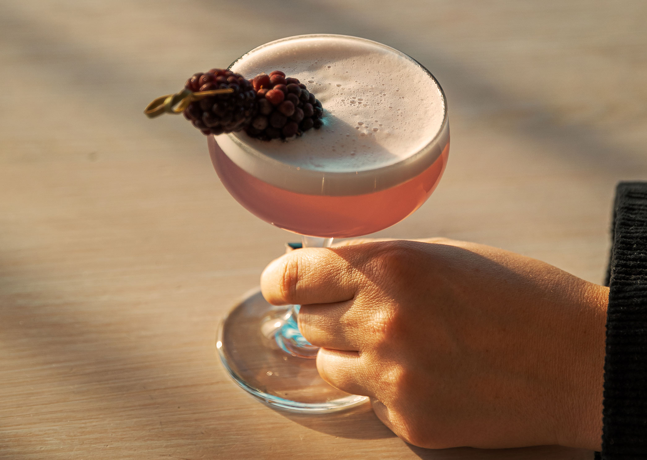 Hand som håller en rosa drink med skum och björnbärsgarnering, serverad på Heaven 23.